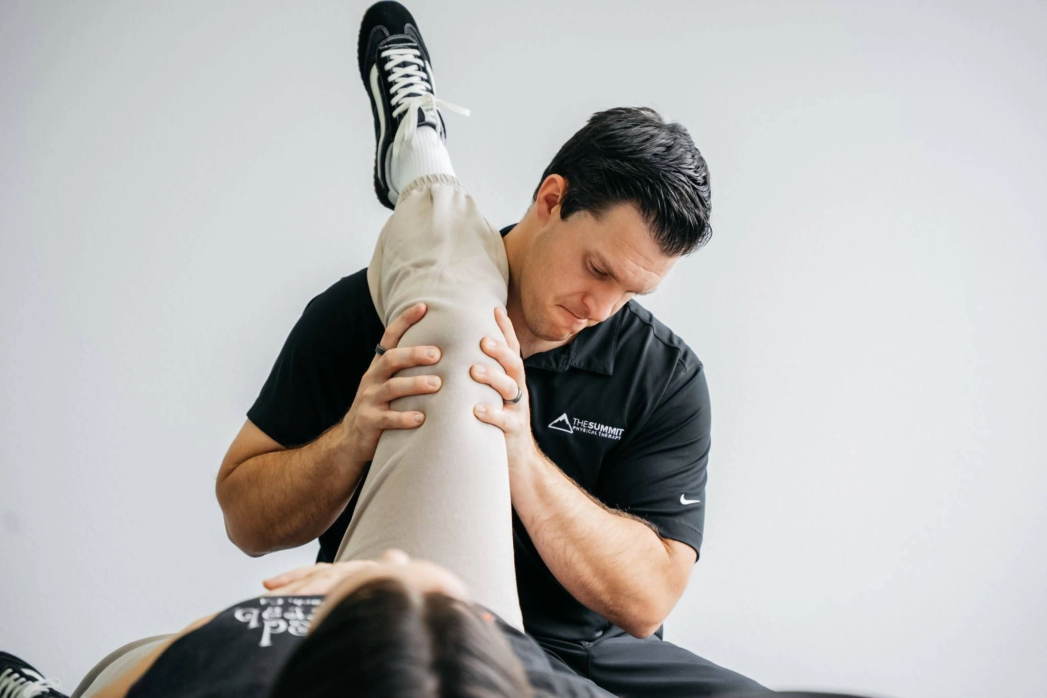 Physical therapist at The Summit PT performing a hip and hamstring stretch during a treatment session.